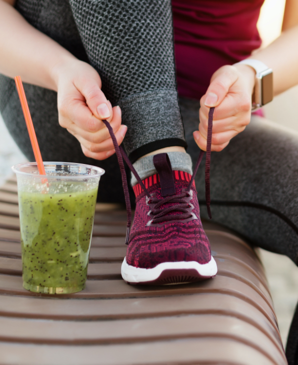 Woman sitting tying shoe lace with healthy drink beside her